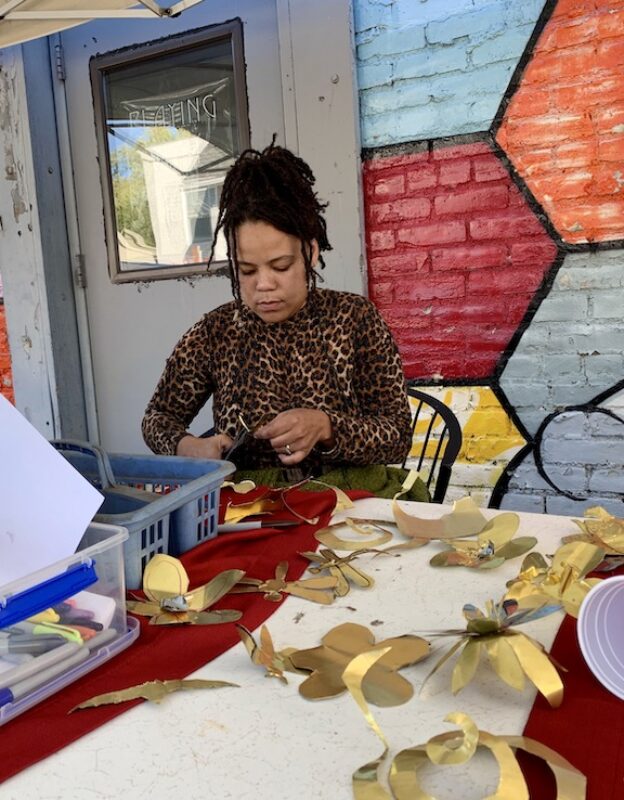 Woman cuts flowers out of metal sheets at community art-making event.