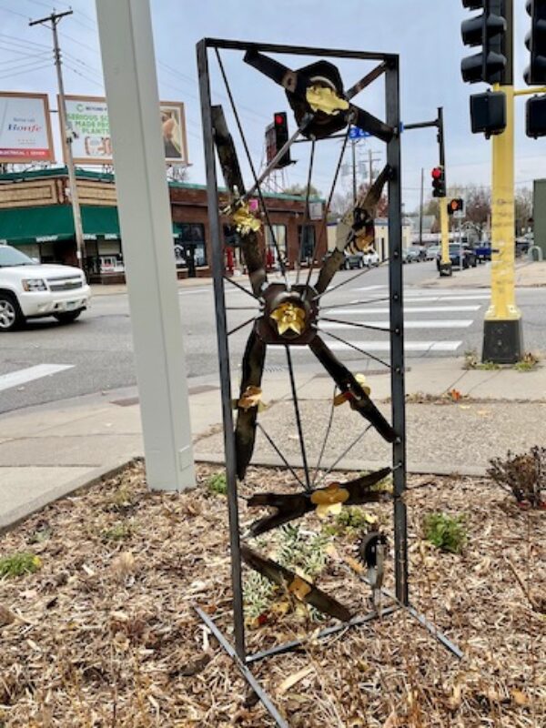 Metal art sculpture featuring flowers and lawnmower blades