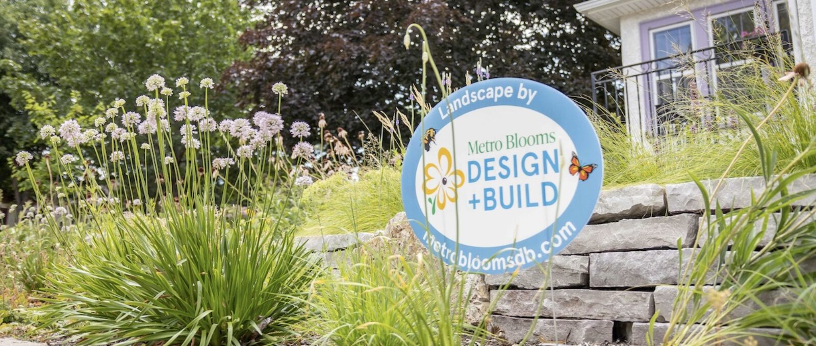 Metro Blooms Design and Build sign in yard with flowers