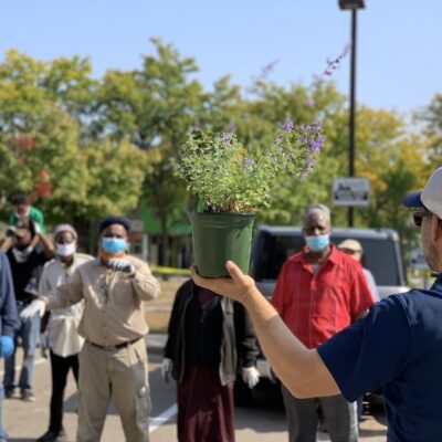 Man holding up potted plant in front of a group of people