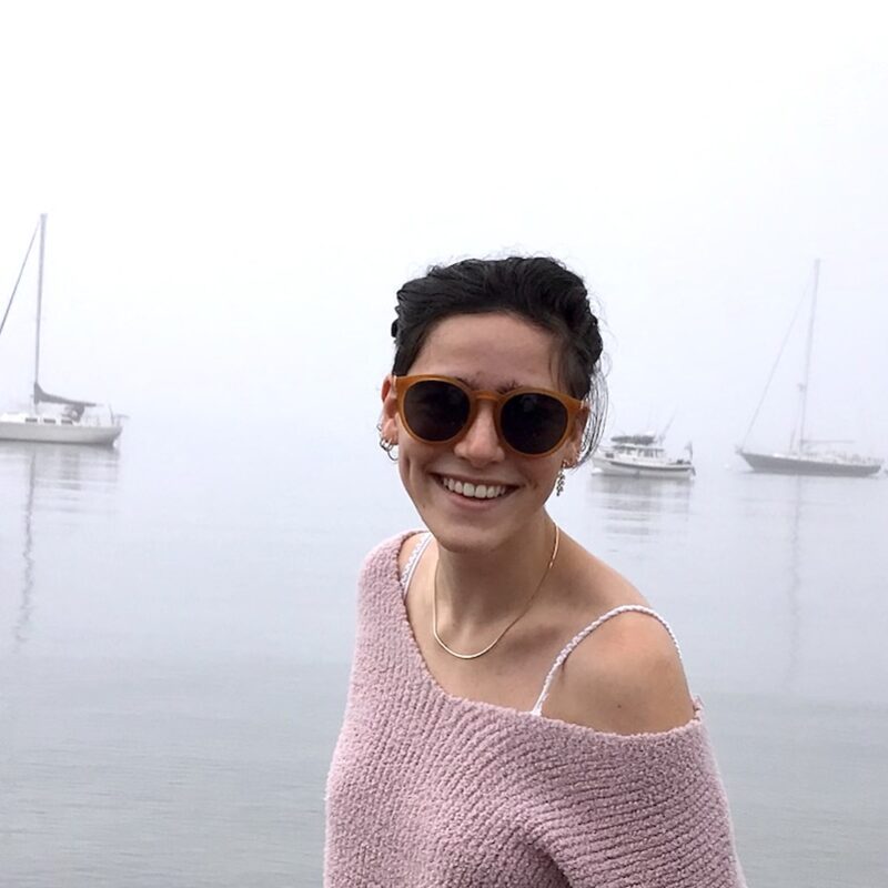 woman in sunglasses in front of lake or ocean with sailboats