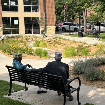 Back of two people on bench in a small park with gardens