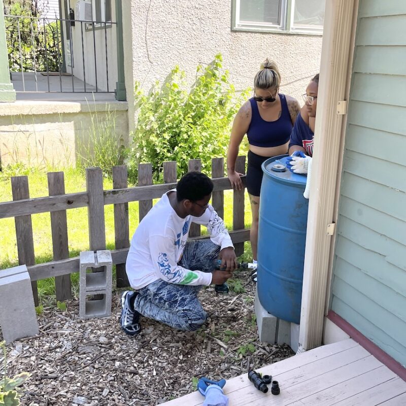 Person installing rain barrel while two others watch