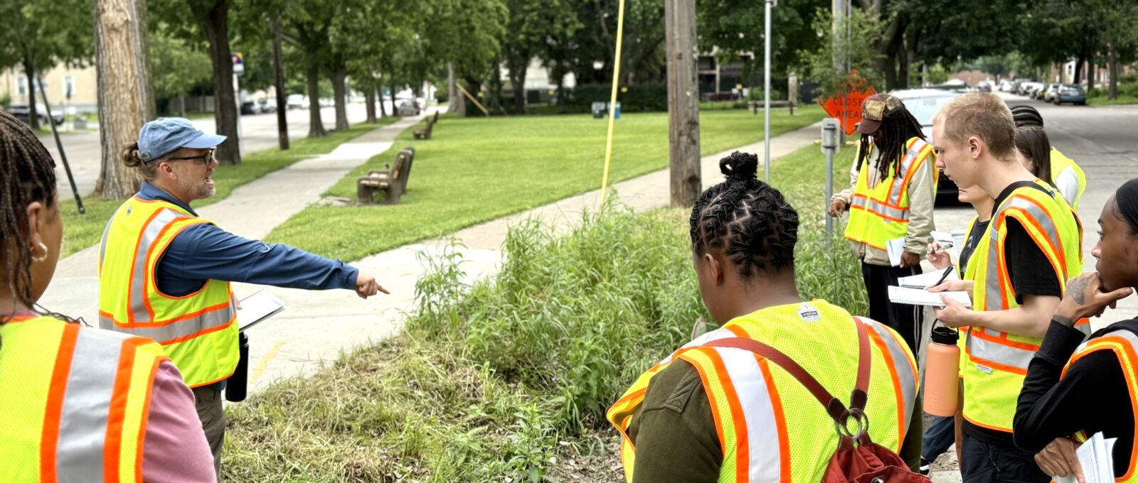 Rich Harrison of Metro Blooms in rain garden pointing out a detail in the garden to landcare training students all wearing yellow vests