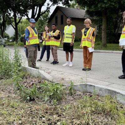 People wearing yellow reflective vests standing in front of rain garden in the early summer discussing the garden
